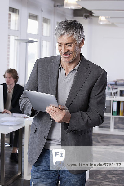Mature man using digital tablet  colleague working in background