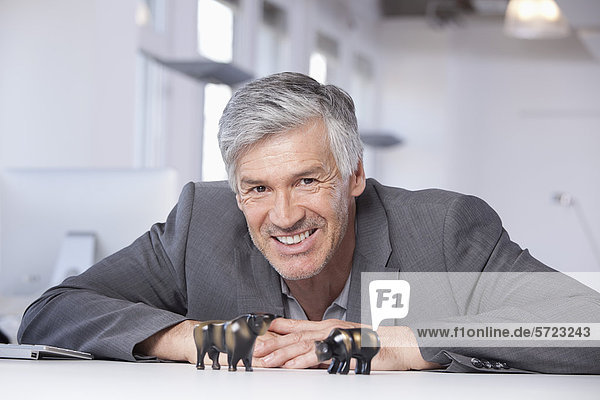 Mature man with bull and bear figurines  smiling  portrait