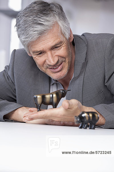 Mature man with bull and bear figurines  smiling