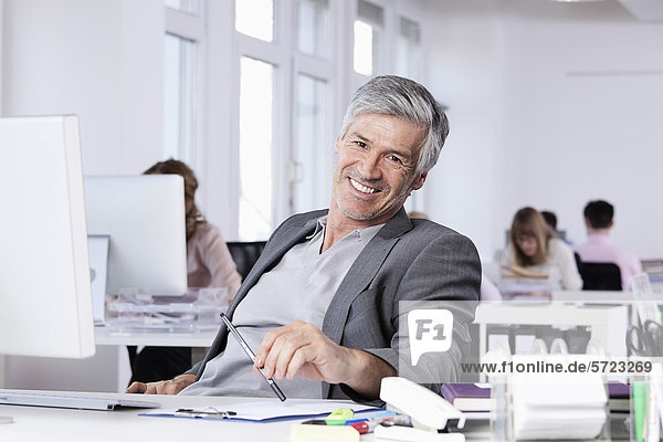 Mature man smiling  colleagues working in background