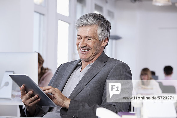 Mature man using digital tablet  colleagues working in background