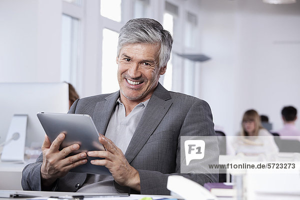 Mature man using digital tablet  colleagues working in background