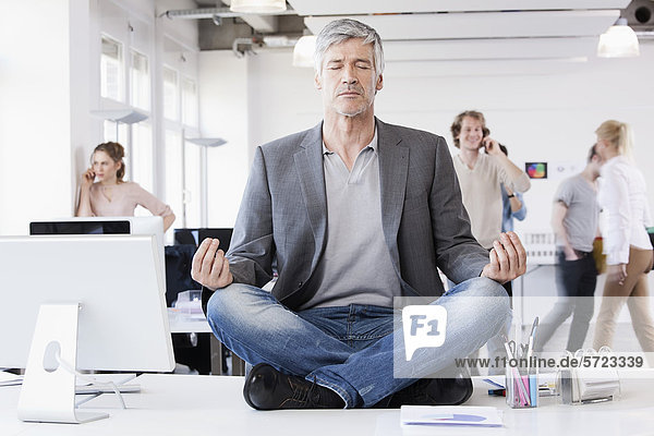Man sitting in lotus position  colleagues in background