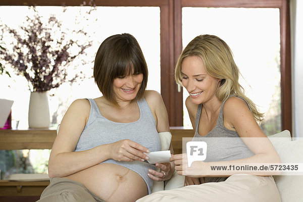 Germany  North Rhine Westphalia  Pregnant woman showing her friend ultrasound image