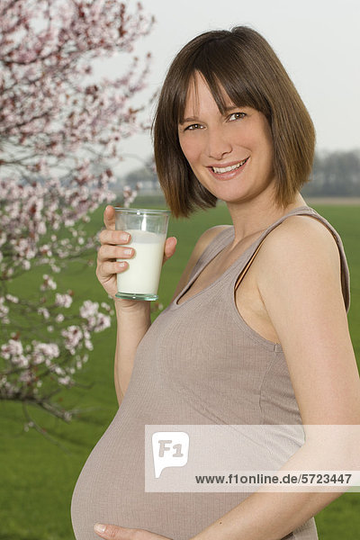 Deutschland  Nordrhein-Westfalen  Schwangere mit Milchglas  lächelnd  Portrait