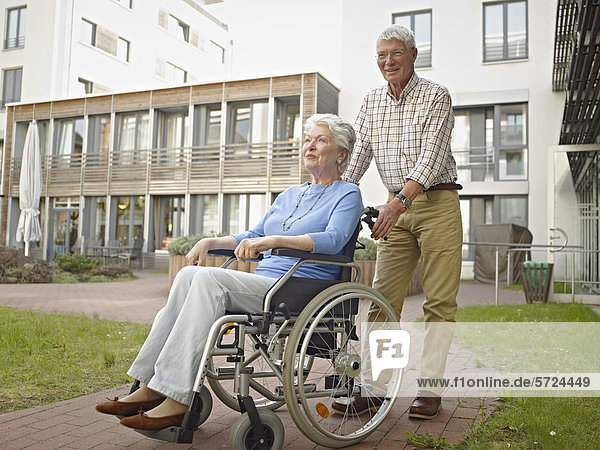 Senior man pushing woman in wheelchair