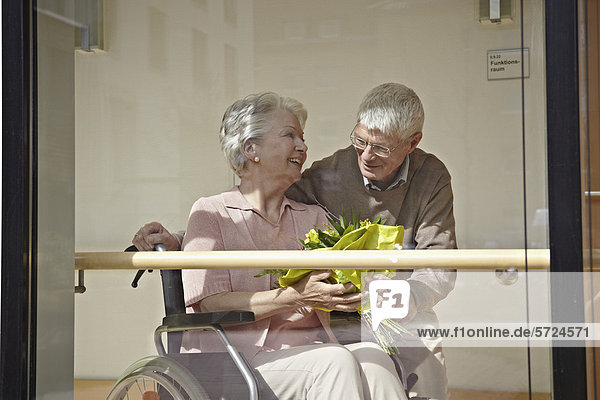 Seniorin im Rollstuhl mit Blumenstrauß  Mann lächelnd