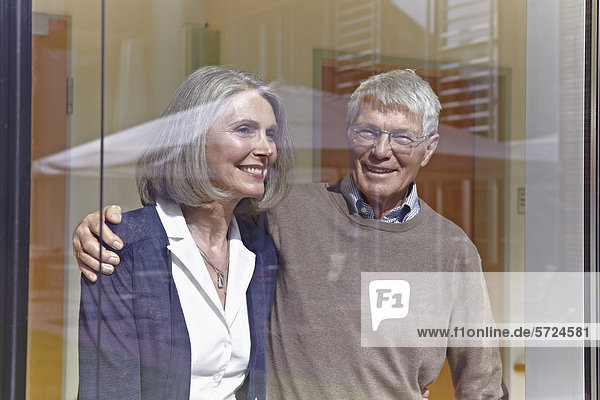 Deutschland  Köln  Seniorenpaar schaut durchs Fenster  lächelnd
