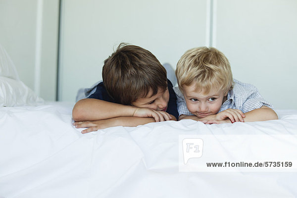 Young brothers lying on bed side by side  heads resting on arms
