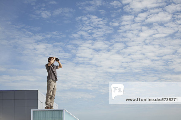 Oversized man standing on rooftop  looking through binoculars