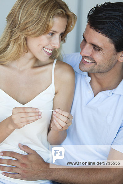 Paar mit Blick auf Schwangerschaftstest  Mann mit Hand auf dem Bauch der Frau