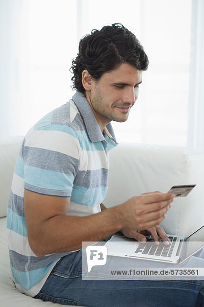 Mittlerer Erwachsener Mann  der eine Kreditkarte hält  während er einen Laptop benutzt.