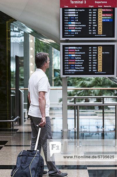 Mann auf der Suche nach Ankunft Abfahrtstafel im Flughafen