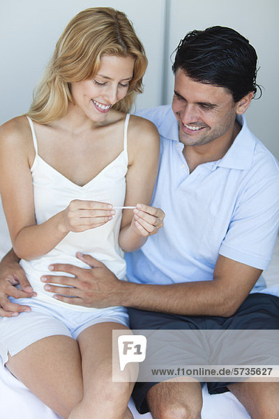 Paar mit Blick auf Schwangerschaftstest  Mann mit Hand auf dem Bauch der Frau