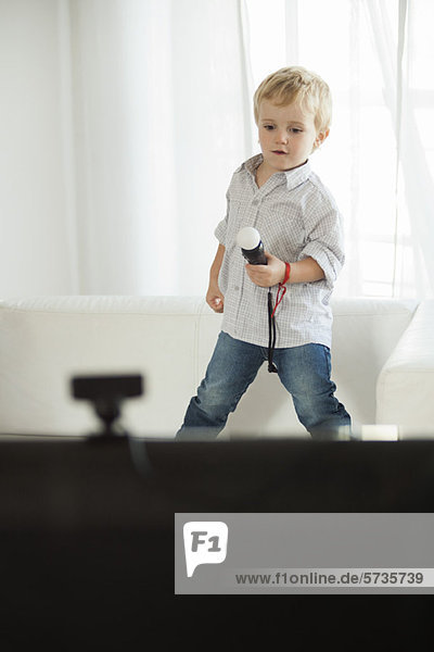 Kleiner Junge steht auf dem Sofa und hält ein Spielzeugmikrofon.