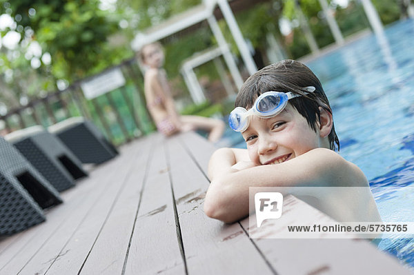 Junge mit Schutzbrille am Rand des Schwimmbeckens  lächelnd