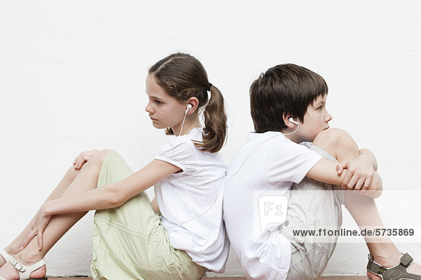 Junge und Mädchen sitzen Rücken an Rücken und hören zusammen Musik.