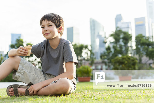Junge sitzt auf Gras im Park  Stadtsilhouette im Hintergrund