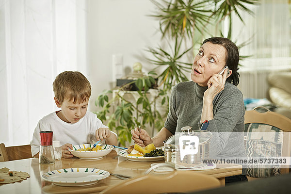 Mother speaking on the phone  sitting at the table with her son