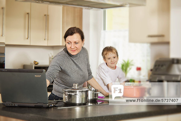 Mutter mit Sohn und Laptop beim Kochen  Multitasking