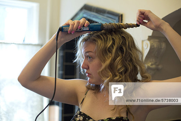 Junge Frau  24  benutzt einen Lockenstab  um ihre Haare zu kräuseln