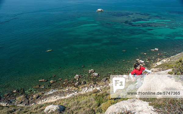 Frau klettert auf felsige Küstenklippe