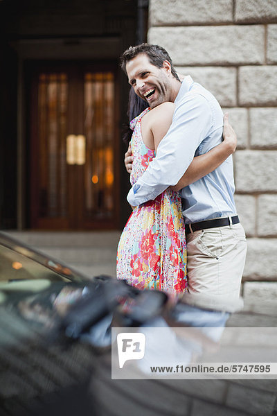 Couple hugging by car on city street