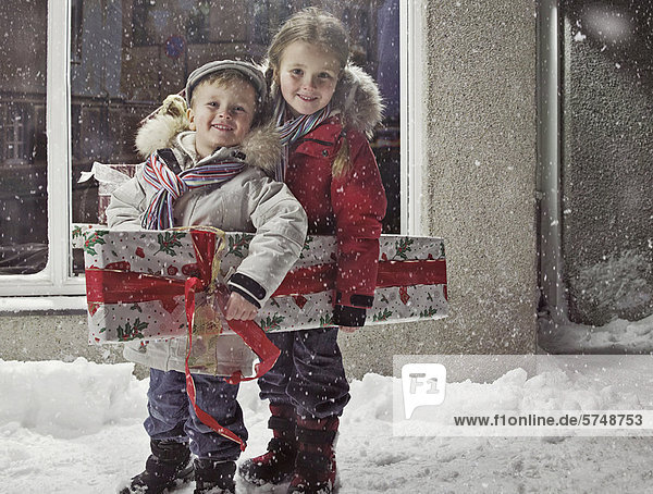 Kinder mit Weihnachtsgeschenk im Schnee
