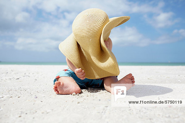 Baby Junge spielt mit dem Sonnenhut der Mutter am Strand