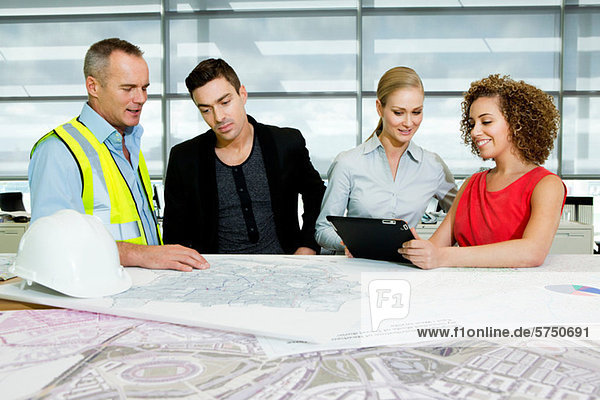 Engineer with architects looking at blueprints and digital tablet in office