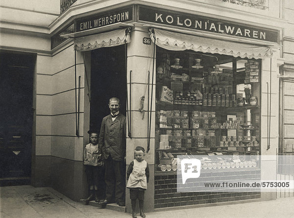 Historische Aufnahme eines Ladenbesitzers vor seinem Lebensmittelladen