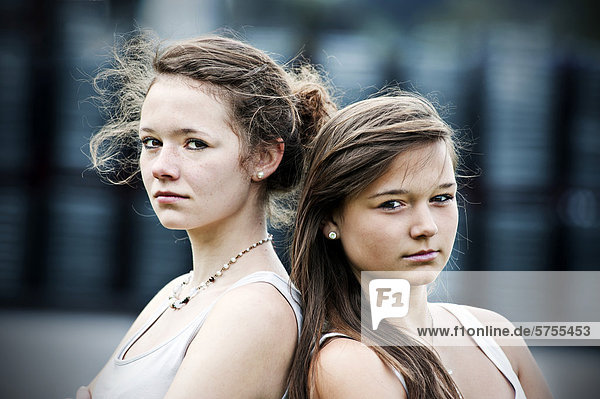 Two teenage girls standing back to back  looking serious