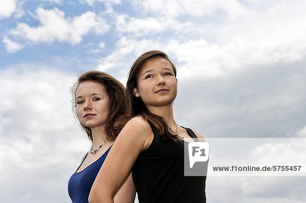 Zwei Mädchen  Teenager  Rücken an Rücken  vor Wolkenhimmel