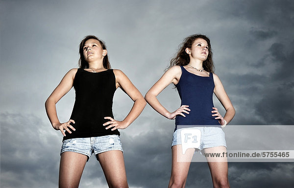Zwei Mädchen  Teenager stehen selbstbewusst vor Gewitterwolken und blicken in die Ferne  Symbolbild  Jugend blickt in die Zukunft