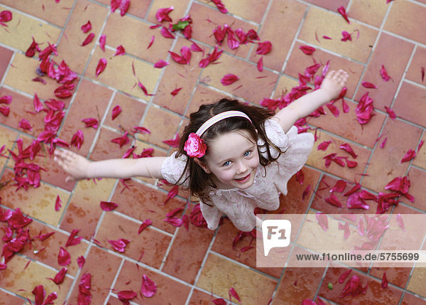 Dreijähriges Mädchen tanzt auf roten Blütenblättern  von oben