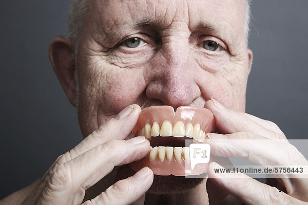 Senior holding false teeth in front of his mouth