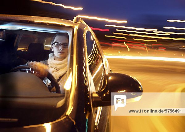 Junge Frau fährt abends mit einem Auto über eine beleuchtete Straße
