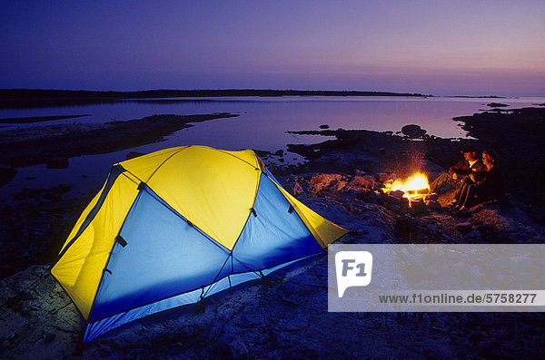 Campers enjoy a campfire at sunset  on the shore of Lake Huron  near Tobermory  Ontario  Canada.