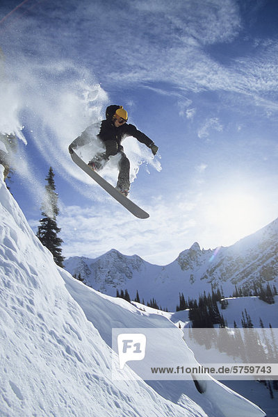 A snowboarder catching air of rock cliff in the backcountry in Golden  British Columbia  Canada.