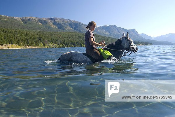 A young woman and her horse wade in the shallow  clear waters of Tatlayoko Lake  British Columbia  Canada