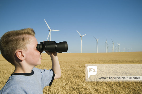 Boy on wind farm looking through binoculars