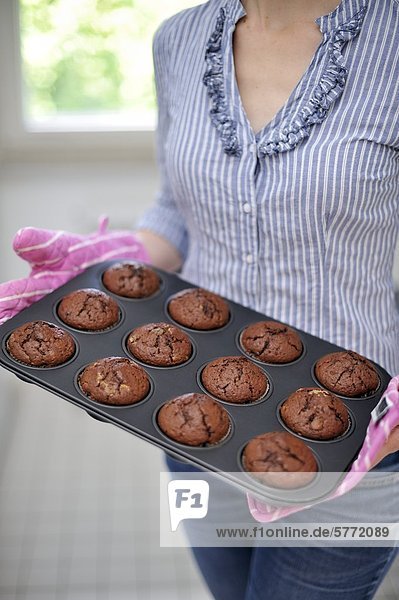 Frau hält ein Backblech mit Muffins