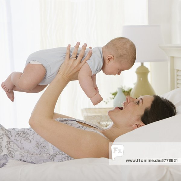 Mother playing with baby on bed
