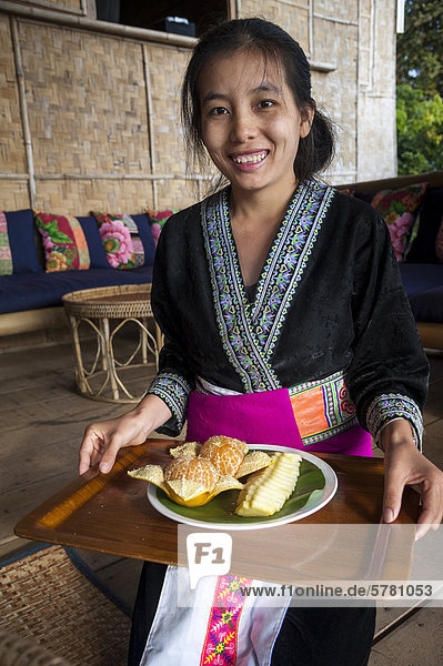Traditionell gekleidete lächelnde Kellnerin mit Obstteller  Frau aus dem Bergstamm oder Bergvolk Schwarze Hmong  ethnische Minderheit aus Ostasien  Nordthailand  Thailand  Asien