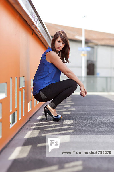 Junge Frau mit blauem Top  schwarzen Leggins und hohen Schuhen auf Brücke