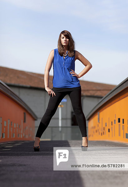 Young woman wearing a blue top  black leggings and high heels on a bridge