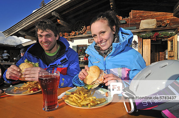 Skifahrer essen Almburger vor Stallenalm  Skigebiet Steinplatte  Reit im Winkl  Chiemgau  Bayern  Deutschland  Tirol  Österreich  Europa