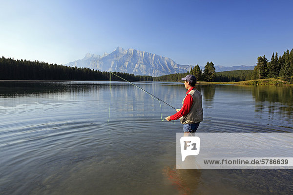 Middle age male fly fishing in mountain lake. Two Jack Lake with Rundle Mountain background  Banff National Park  Alberta  Canada.