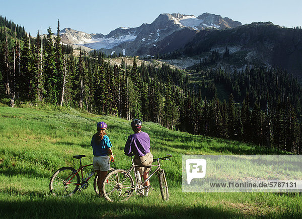 Young couple rest on bikes in meadow  Whistler Peak  British Columbia  Canada.