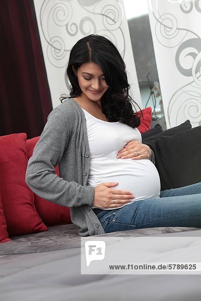 Schwangere Frau auf der Couch hält ihren Bauch